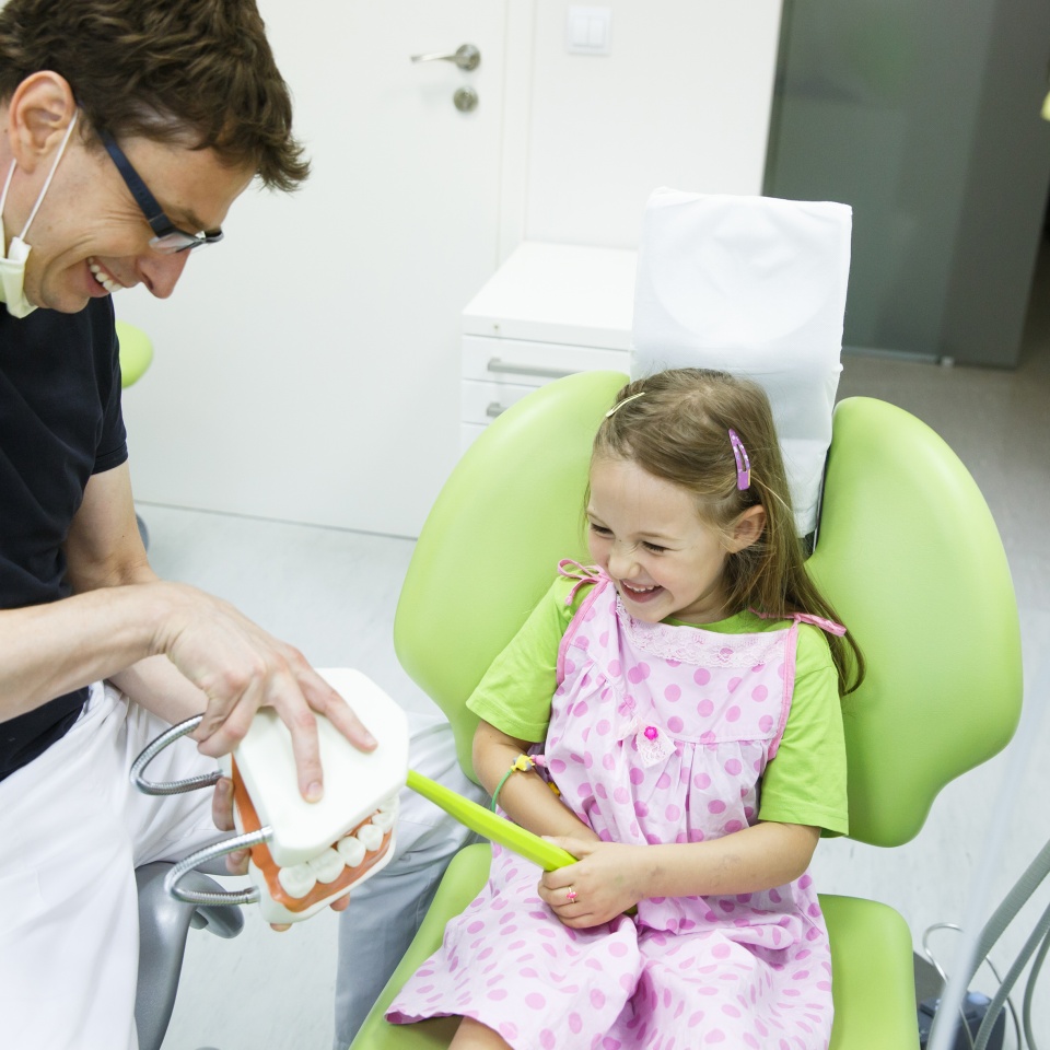 Smiling little girl having fun with her pediatric dentist brushing a dental model being educated about proper tooth-brushing. Early prevention oral hygiene demonstration concept.