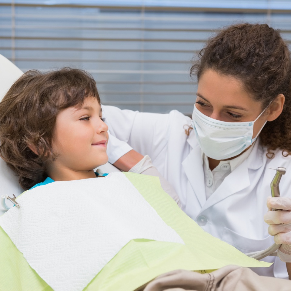 Pediatric dentist showing little boy in chair the drill at the dental clinic