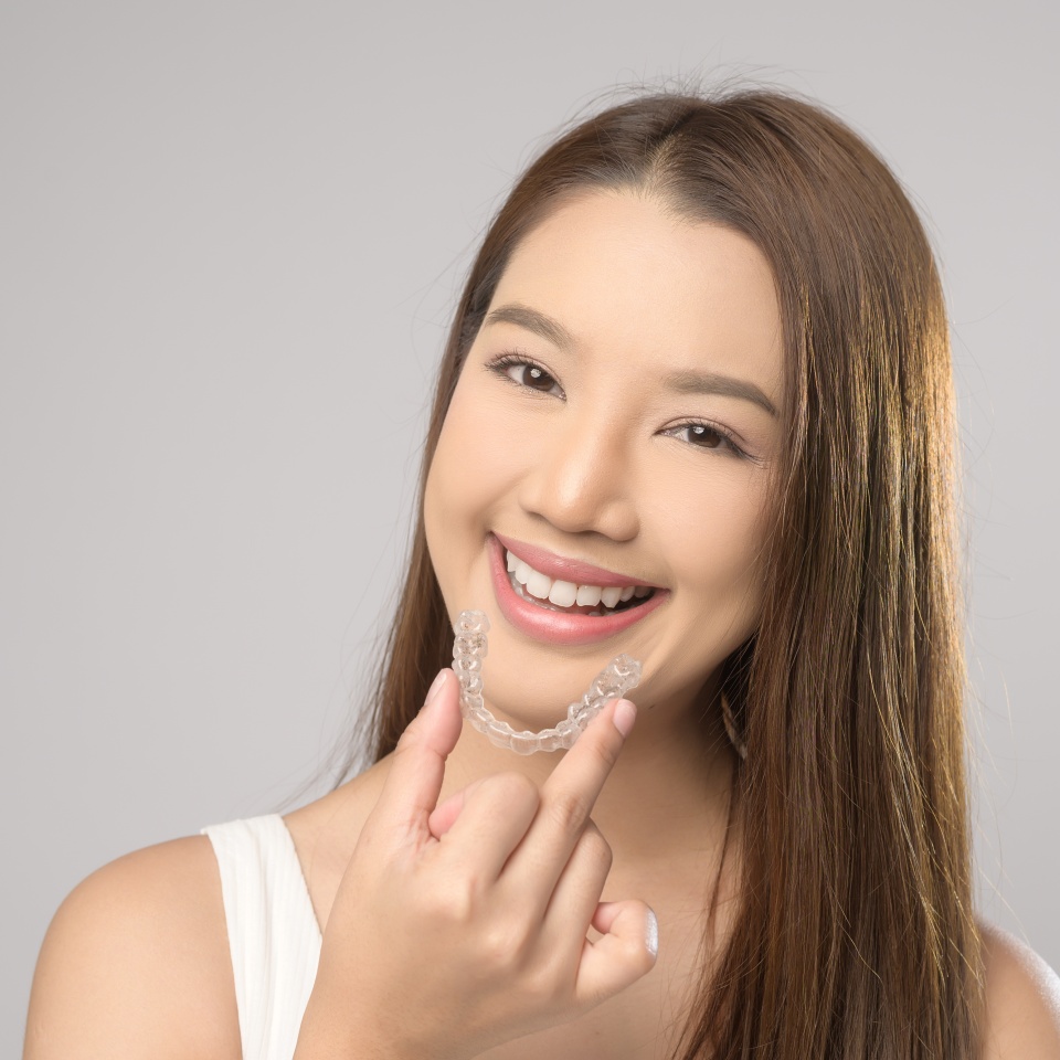 A Young smiling woman holding invisalign braces over white background studio, dental healthcare and Orthodontic concept.